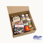 Cardboard box with Colombian food items and books on a white background