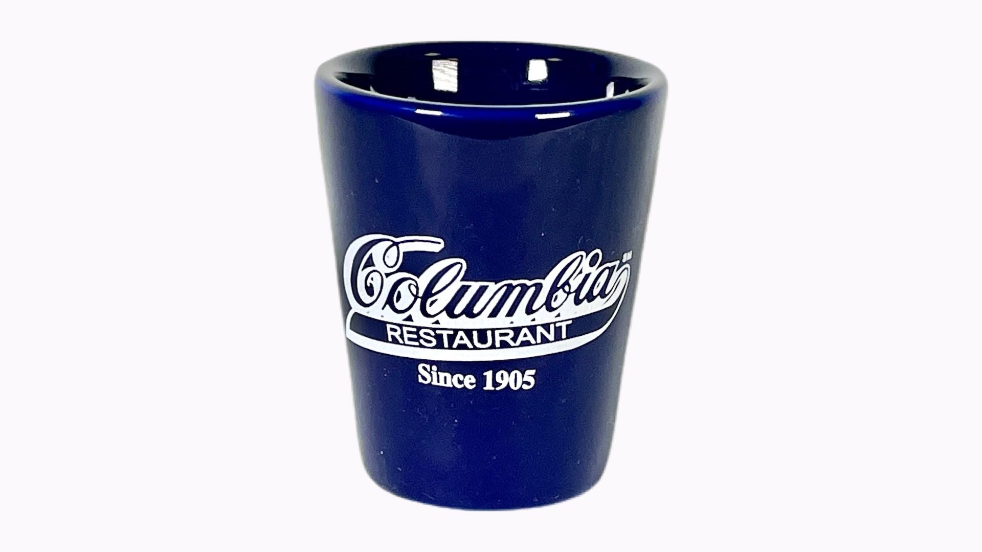 A blue shot glass with the Columbia Restaurant logo printed on it.