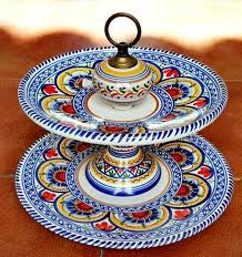 A two-tiered serving tray with brightly colored floral and geometric patterns on a red background, with a black handle on top.